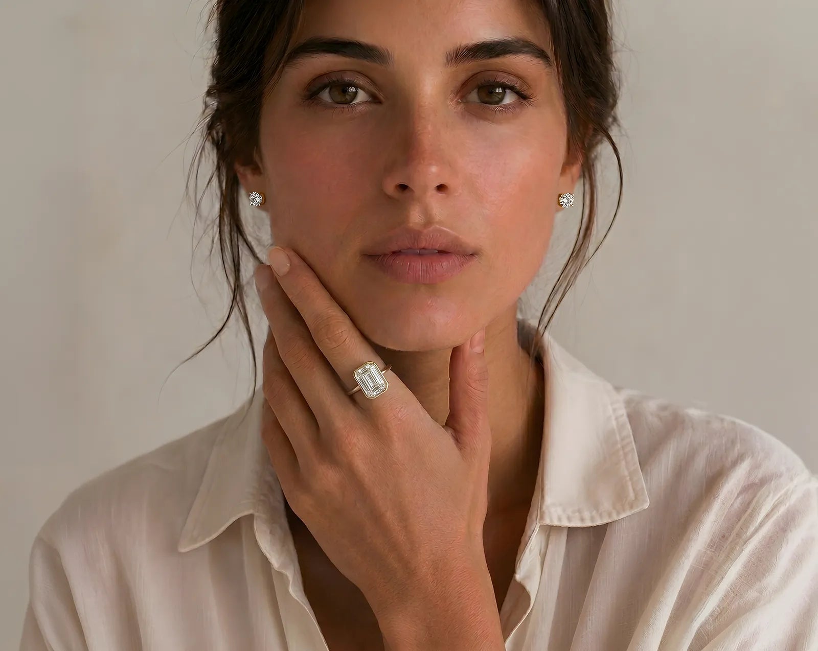 Woman wearing a diamond ring and earrings against a neutral background