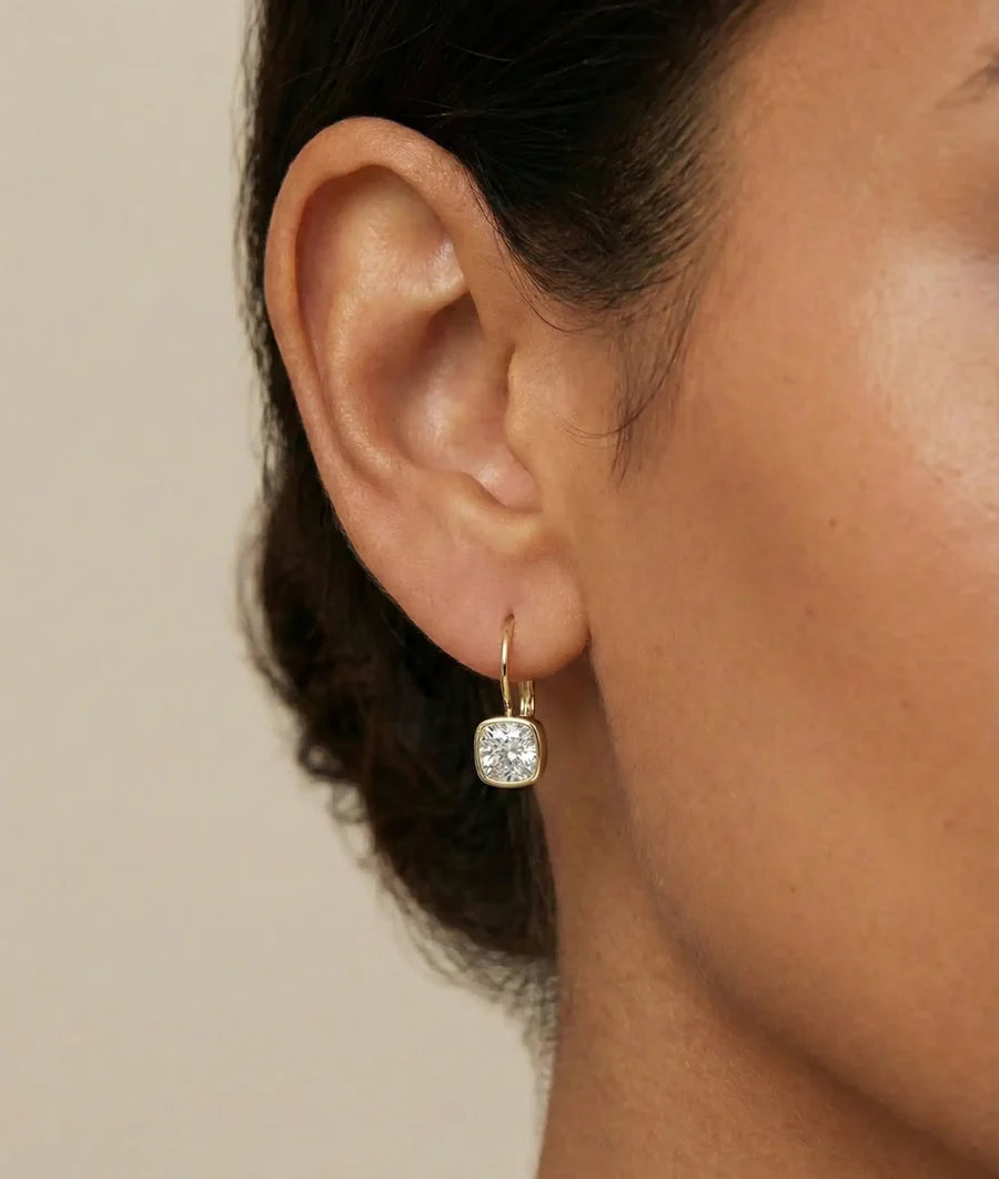 Model wearing bezel cushion diamond drop earrings in yellow gold
